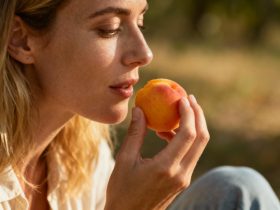 Jeune femme européenne souriante mangeant quelques abricots frais posés sur une table en bois