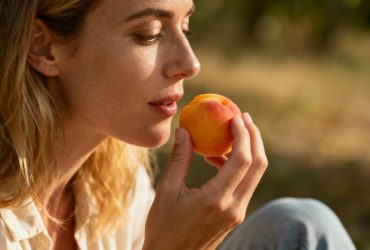 Jeune femme européenne souriante mangeant quelques abricots frais posés sur une table en bois